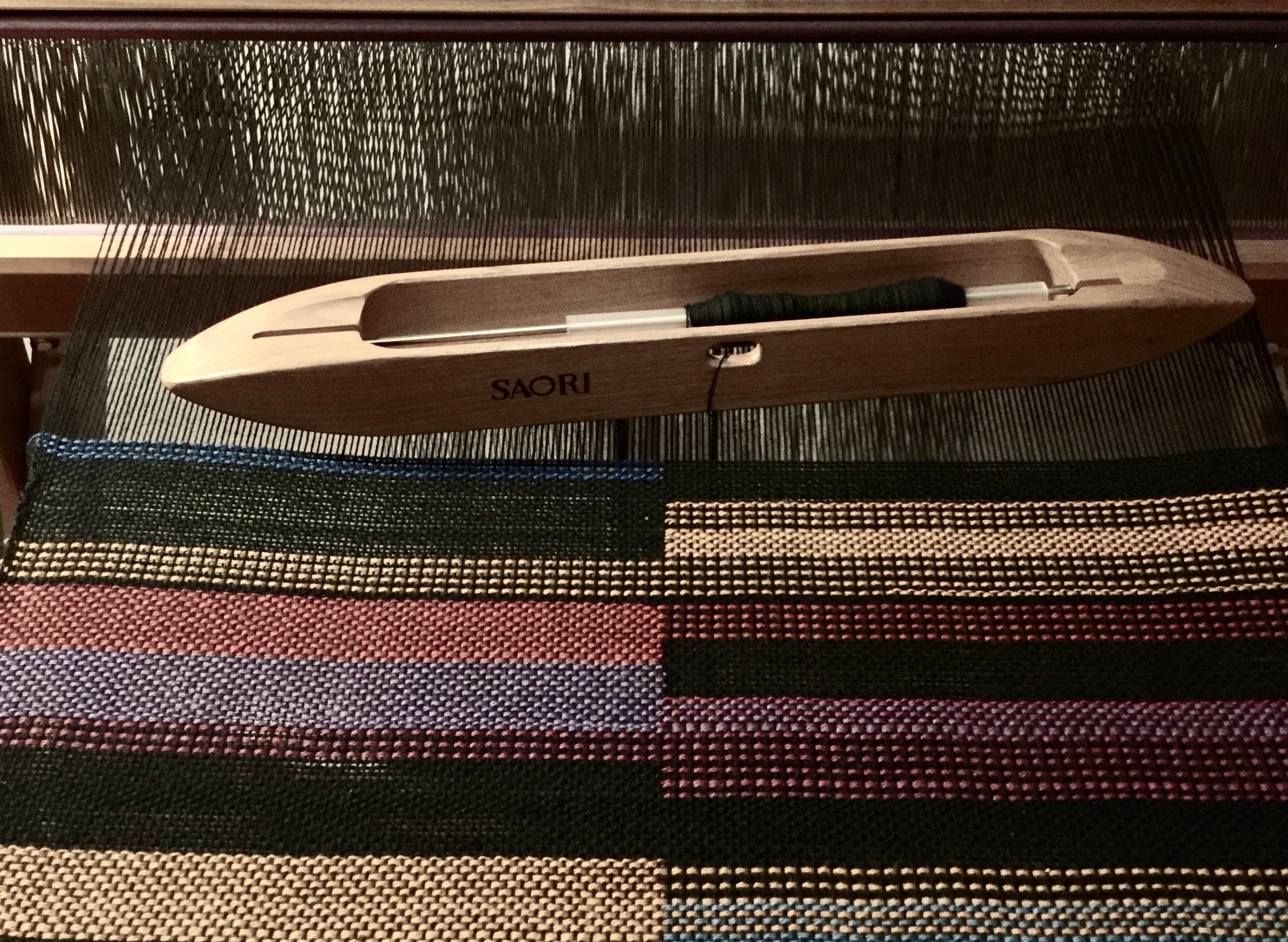 Translation missing: en.A shuttle of cotton sitting on a Saori hand loom with some hand weaving